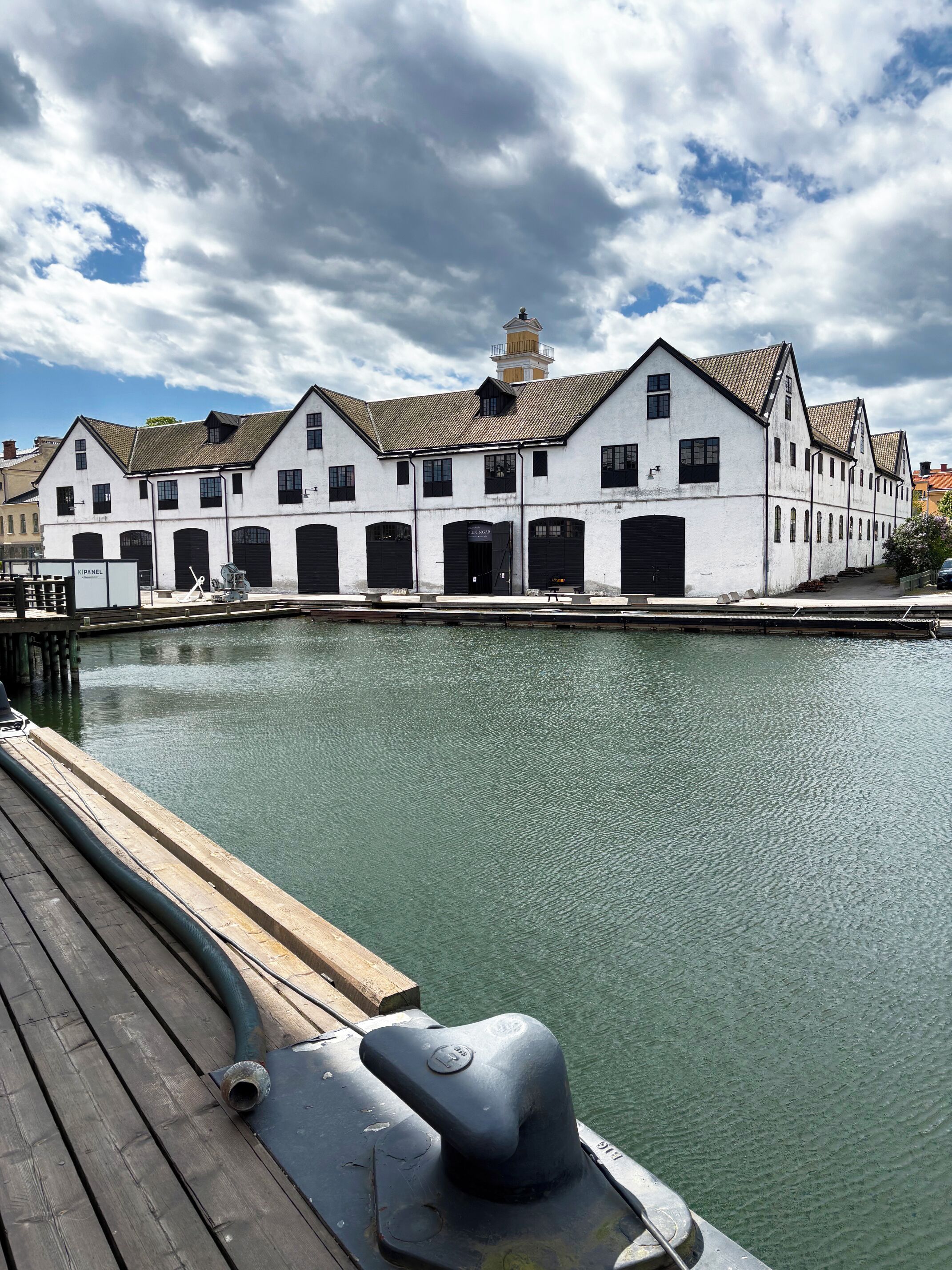Un edificio frente al agua con varias puertas y ventanas negras, un muelle con una manguera y un cielo nublado.