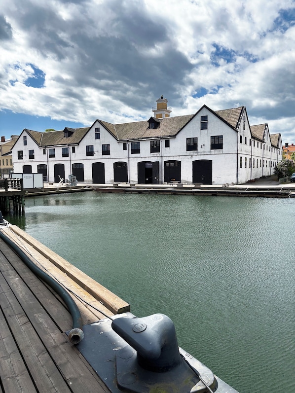 A waterfront building with multiple black doors and windows, a dock with a hose, and a cloudy sky.