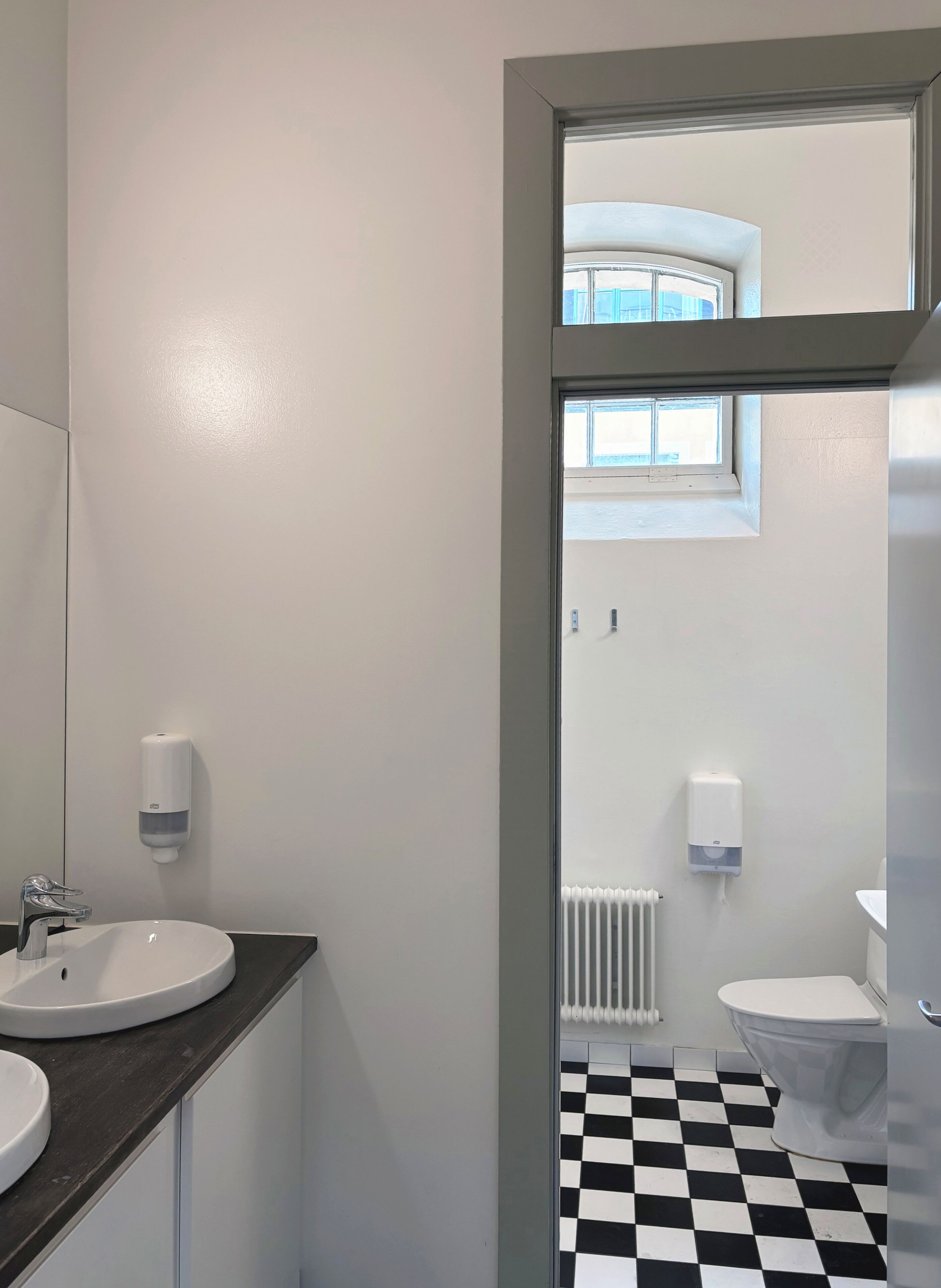 A bathroom with a black and white checkered floor, a white sink, and a window above the toilet.