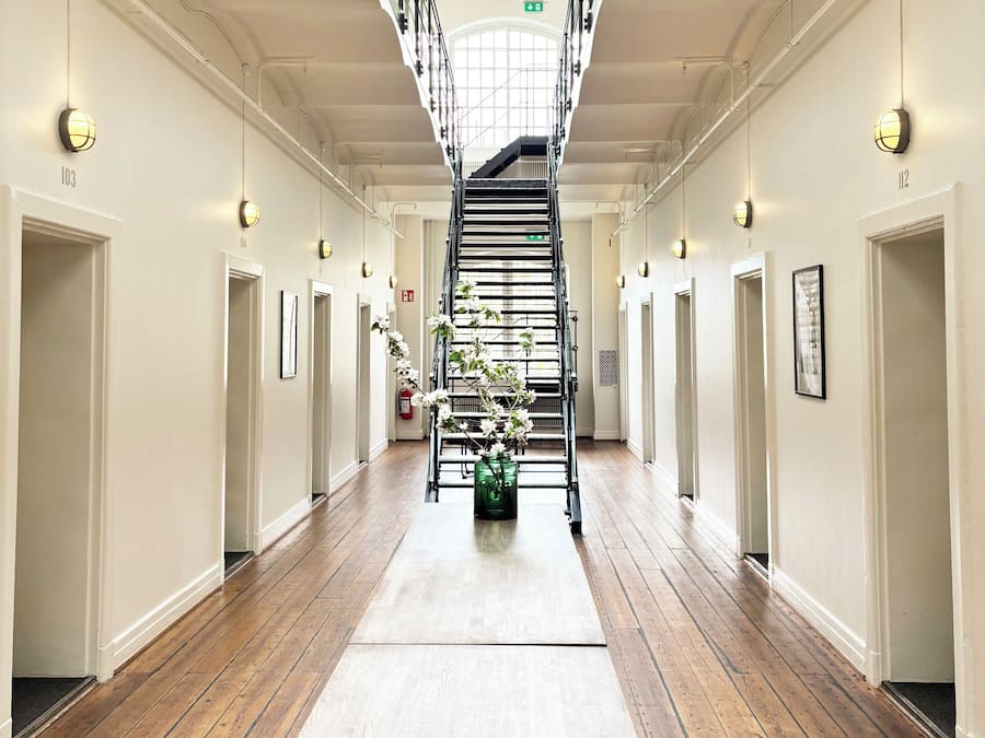 A hotel corridor with a central staircase, wooden flooring, and a skylight.
