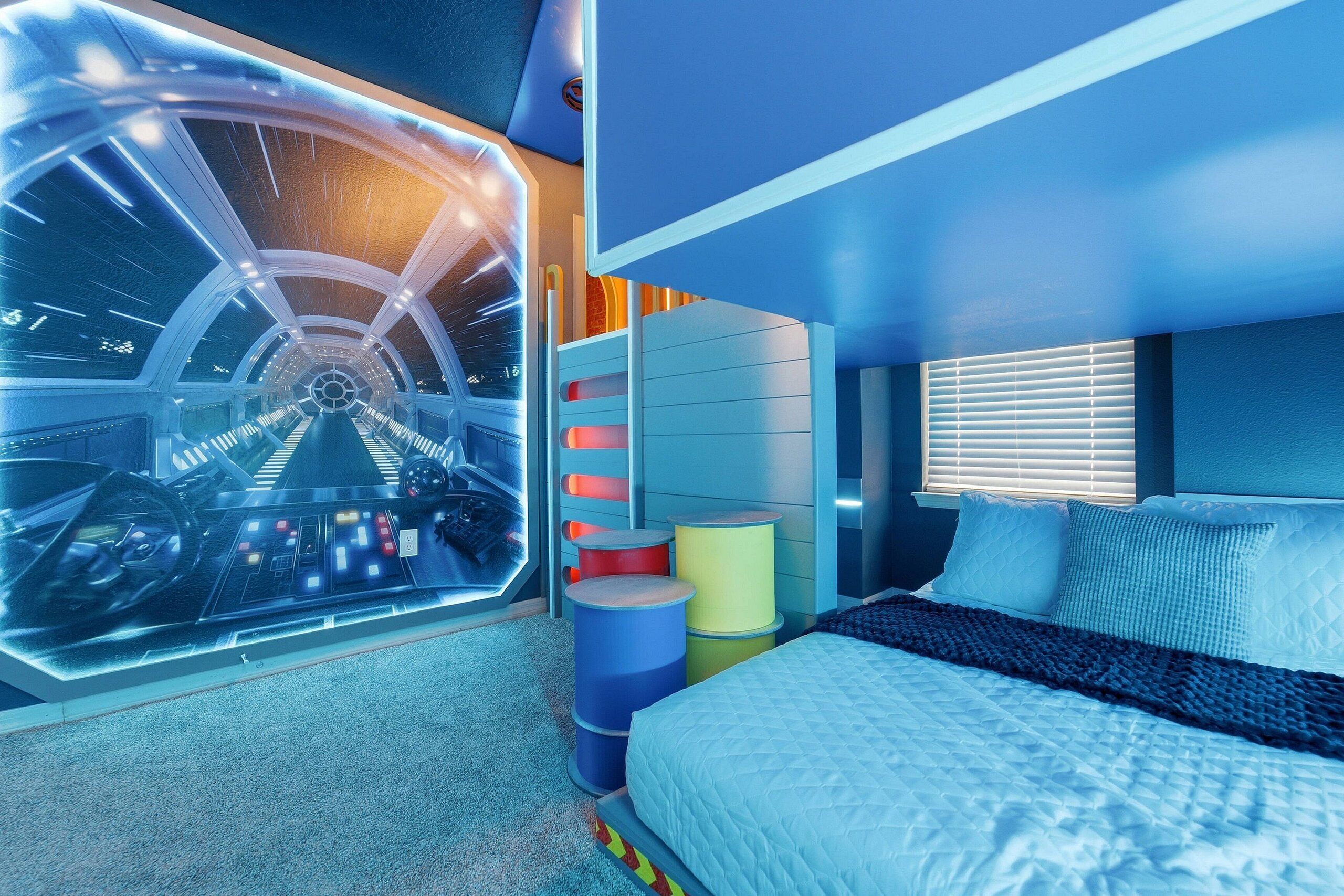 Un dormitorio con cama, ventana con persianas, televisor montado en la pared y un ventanal con vistas a una habitación temática del espacio.