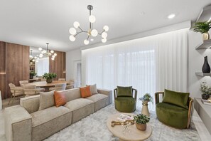 Ein modernes Wohnzimmer mit einer Eckcouch, zwei Sesseln, einem Couchtisch und einem Essbereich im Hintergrund.