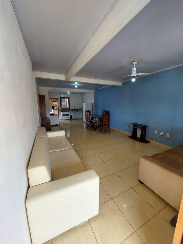 A spacious living area with a sofa set, a dining table, and a kitchen in the background.