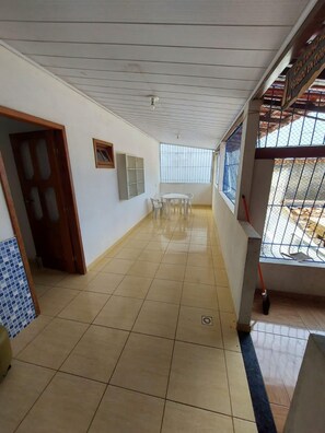 A hallway with tiled flooring, a dining area with chairs and a table, and a window with metal bars.