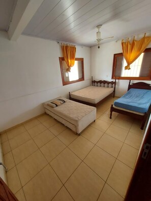 A room with two beds, a ceiling fan, and a window with curtains.