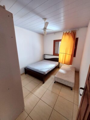 A room with a bed, a small table, a ceiling fan, and a window with curtains.