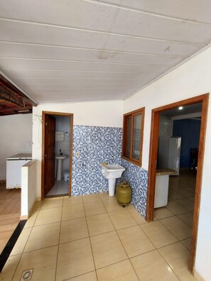 A small, open-plan kitchen and bathroom area with tiled flooring, a sink, and a toilet.