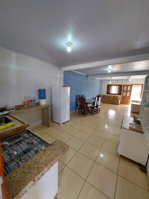 A kitchen with a gas stove, a refrigerator, and a dining area with chairs and a table.