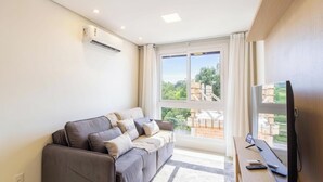 Ein modernes Wohnzimmer mit grauem Sofa, einem Flachbildfernseher und einem großen Fenster mit Blick auf eine Baustelle.