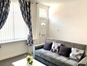 A living room with a grey sofa, a white coffee table, and a door with a window. - Amazing 2-bedroom house in enchanting Manchester perfect for your stay (Manchester)