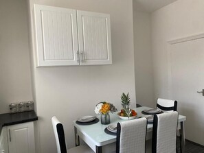 A dining area with a white table, black chairs, a white cabinet above, and a door to the right. - Amazing 2-bedroom house in enchanting Manchester perfect for your stay (Manchester)