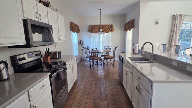 Una cocina moderna con armarios blancos, una isla central y un comedor con candelabro.
