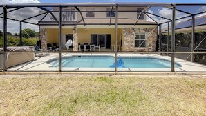Piscina techada al aire libre con zona de patio, pared de piedra y un edificio de dos pisos al fondo.