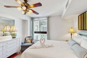 Ein Hotelzimmer mit Bett, Deckenventilator, Fenster mit Blick, Kommode und Lampen.