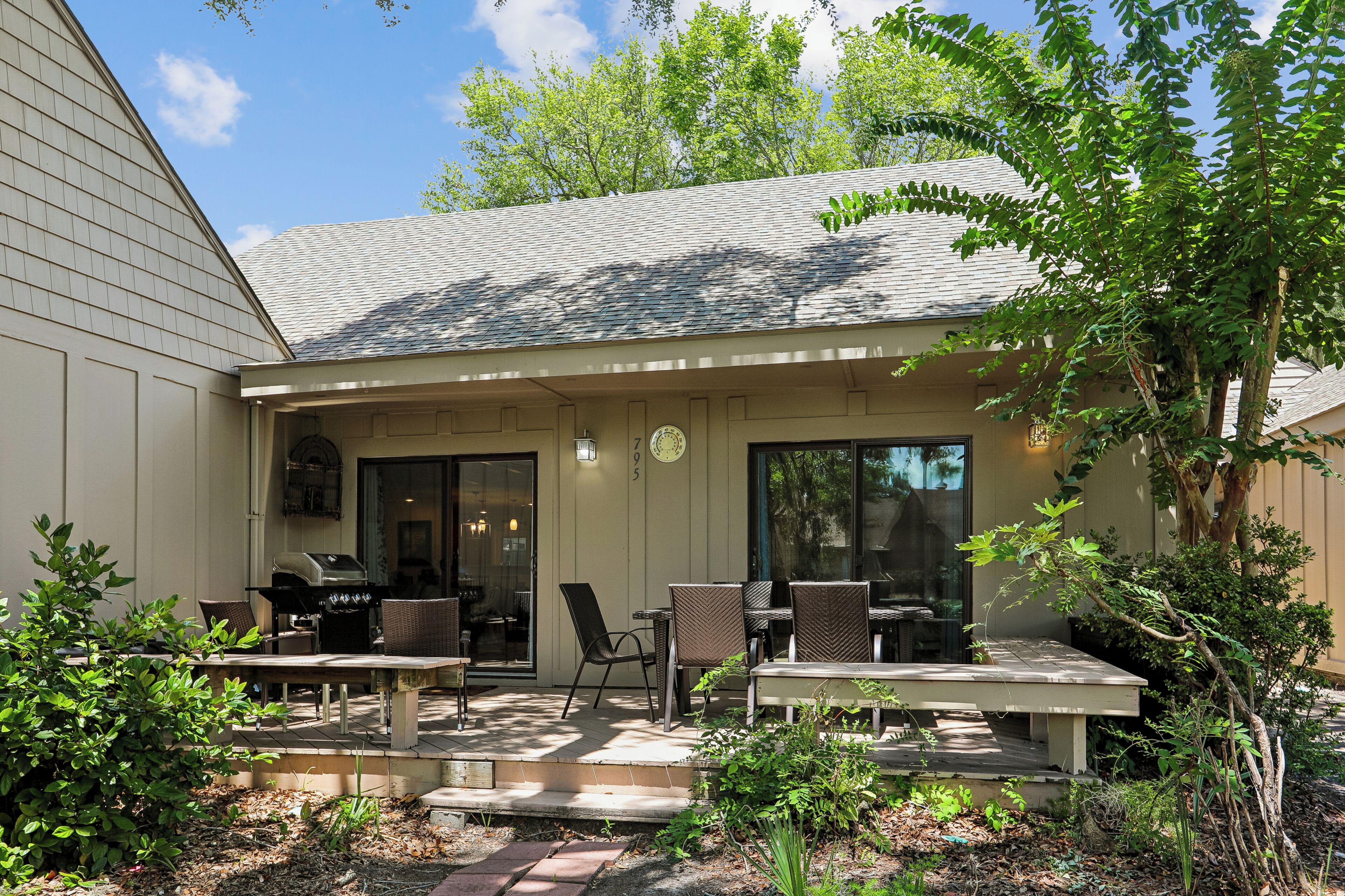 Un patio couvert avec un espace extérieur aménagé pour s’asseoir, un barbecue et une porte donnant accès à un espace intérieur.