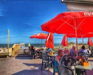 Ein Restaurant direkt am Strand mit Terrassenplätzen, roten Sonnenschirmen und Meerblick.
