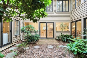 A residential building with a covered patio, a small garden with stepping stones, and a view of the interior through the glass doors. - Beautiful Home w/ Private Pool & Spa (Hilton Head Island)