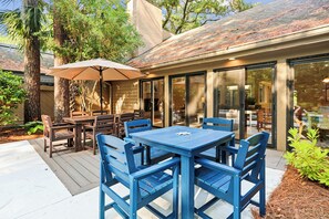 Eine Terrasse im Freien mit Tisch und Stühlen, einem großen Sonnenschirm und einem eingezäunten Essbereich aus Glas.