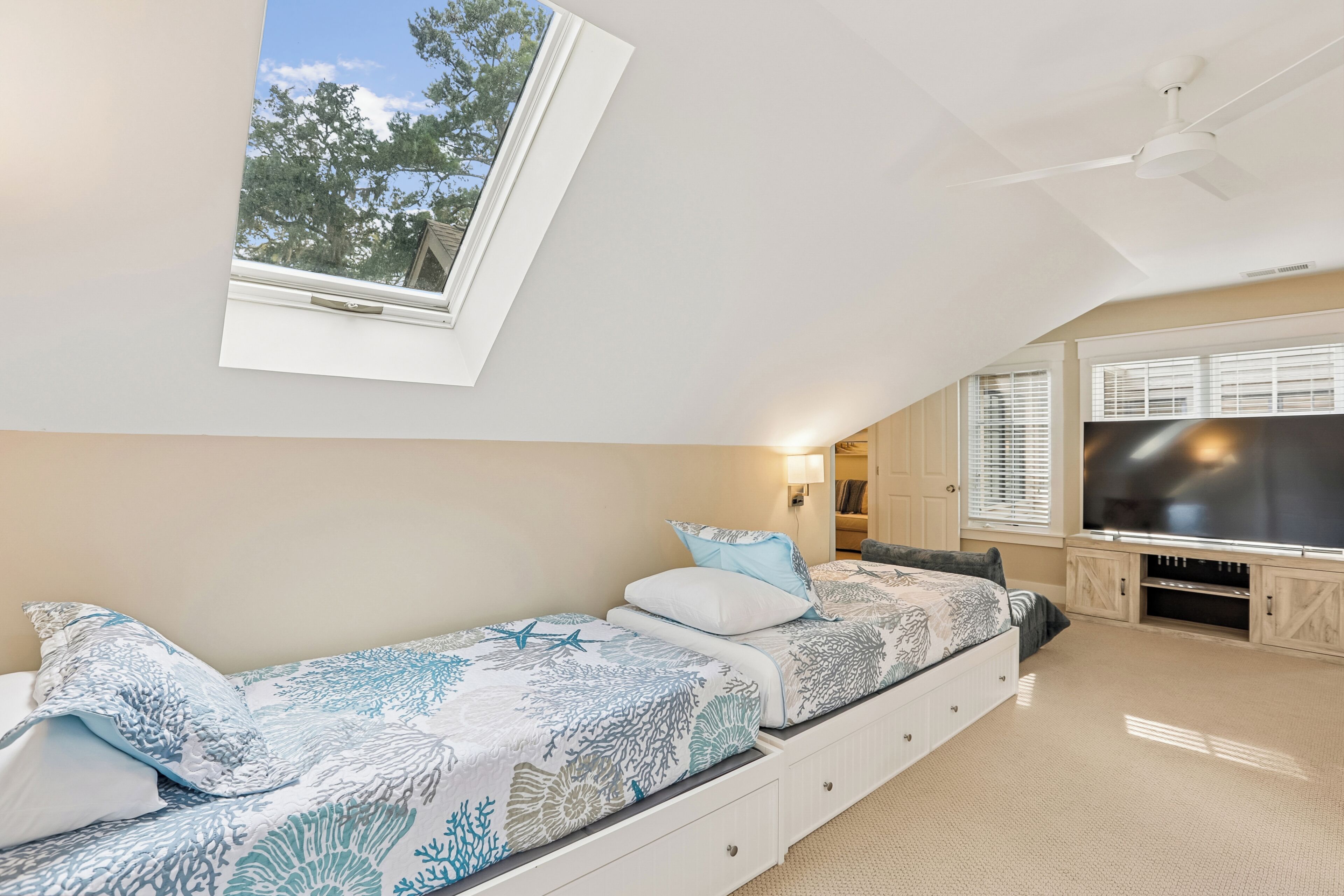A bedroom with a bed, a ceiling fan, a TV, and a window with a view of trees.