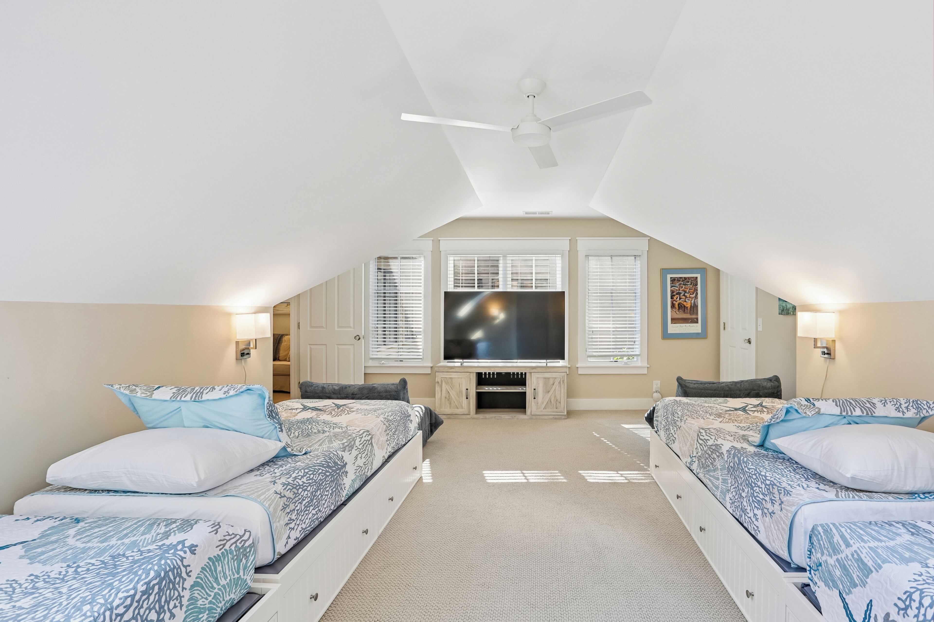 A bedroom with two beds, a ceiling fan, a television, and a fireplace.
