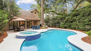 Um quintal com piscina, um alpendre coberto com móveis de exterior e uma casa com telhado em tijolos.