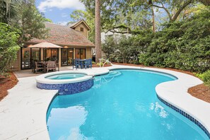 Ein Garten mit Swimmingpool, einer überdachten Terrasse mit Gartenmöbeln und einem Haus mit Ziegeldach.