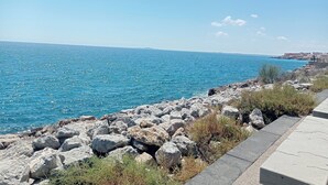 A coastal view with a rocky shoreline, clear blue sea, and distant buildings. - STUDIO 30 M FROM THE BEACH AND NEAR SHOPS AND BUS STOPS (Sète)