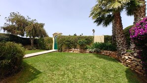 A well-maintained garden with a stone wall, palm trees, and a variety of shrubs. - Villa lote 10 Paraiso da luz T4 (Luz)
