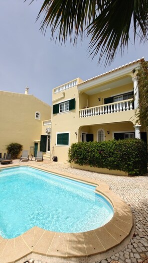 A two-story building with a swimming pool, a balcony, and a tiled patio area. - Villa lote 10 Paraiso da luz T4 (Luz)