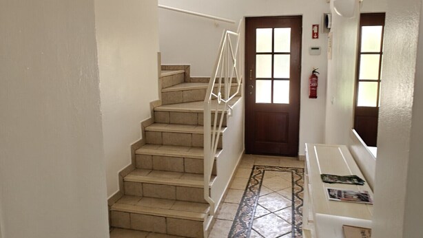 A hallway with a staircase, a door, a fire extinguisher, and a small refrigerator. - Villa lote 10 Paraiso da luz T4 (Luz)