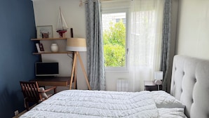 Un dormitorio con cama, escritorio, silla, lámpara y ventana con cortinas.
