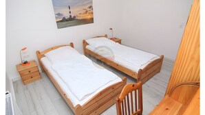 Una camera da letto con due letti in legno, un comodino con una lampada, un piccolo cassetto e un quadro appeso al muro.