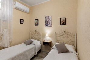 Una habitación con dos camas, una mesita de noche con lámpara y aire acondicionado de pared.