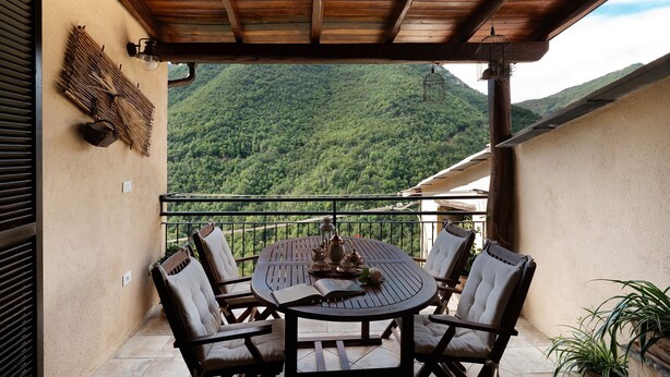 Un balcón con techo de madera, una mesa redonda con sillas y vista a una montaña boscosa.