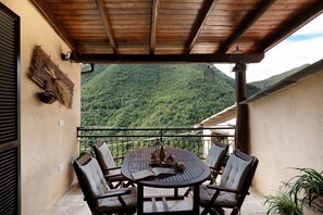 Un balcón con techo de madera, una mesa redonda con sillas y vista a una montaña boscosa.