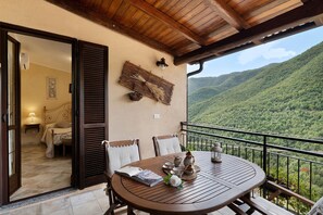 Une table en bois, entourée de chaises, sur un balcon donnant sur un paysage montagneux.