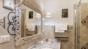 Un baño con un espejo grande, un lavamanos, dos luces empotradas en la pared y una zona de ducha.