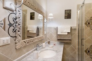 Une salle de bain avec un grand miroir, un lavabo, deux appliques murales et un espace douche.