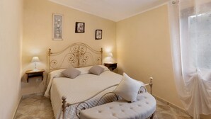 Un dormitorio con cama, mesitas de noche, una ventana con cortinas e imágenes colgadas en la pared.