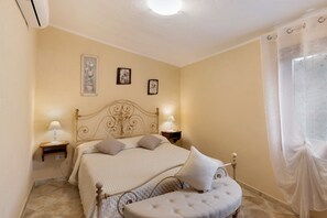 Une chambre à coucher comprenant un lit, des tables de chevet, une commode, une fenêtre avec des rideaux et des tableaux accrochés au mur.