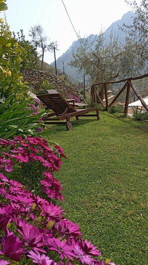 Ein Garten mit einer hölzernen Bank, einer Steinmauer und Blick auf die Berge.