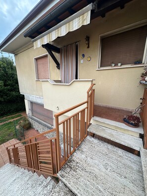 Ein Wohngebäude mit einer Holztreppe, einem Fenster mit einem Streifenmuster-Vorhang und einem kleinen Balkon mit Blumentöpfen.