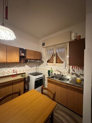 Una cocina compacta con armarios de madera, una estufa blanca, un fregadero y una mesa de comedor.