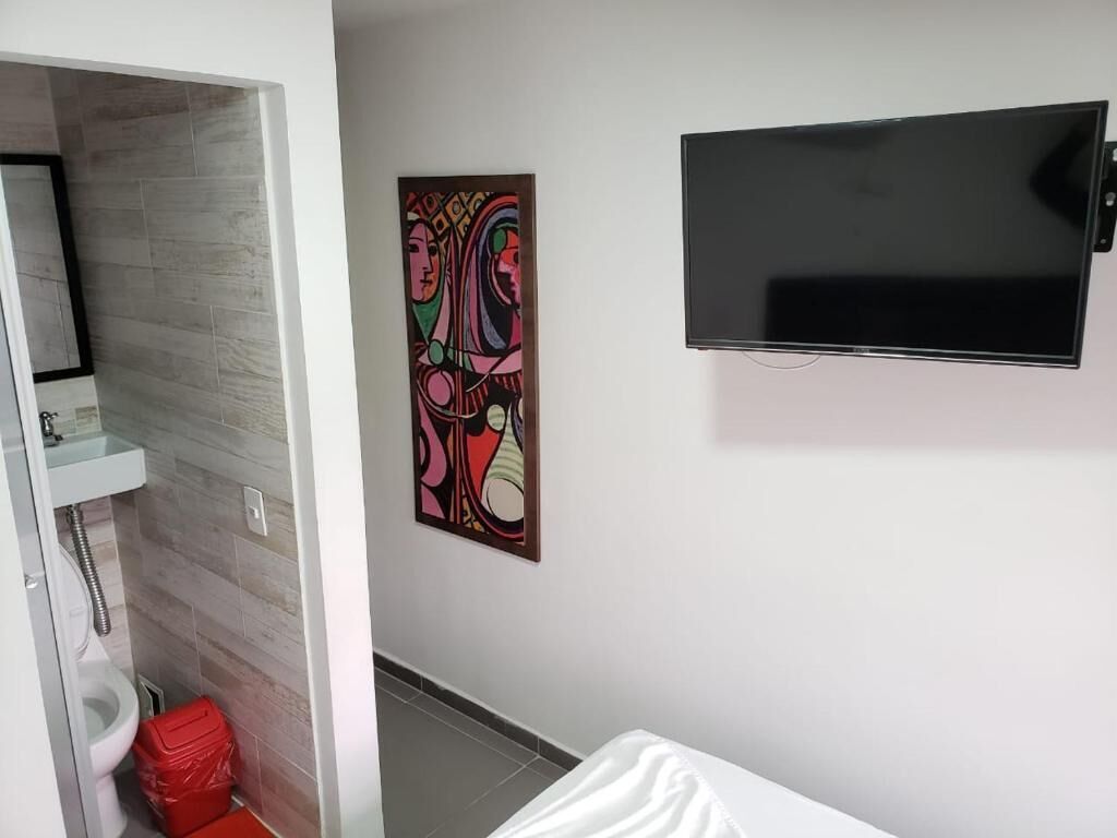 Ein Badezimmer mit Toilette, einer roten Mülltonne, einem weißen Waschbecken und einem an der Wand befestigten Fernseher.