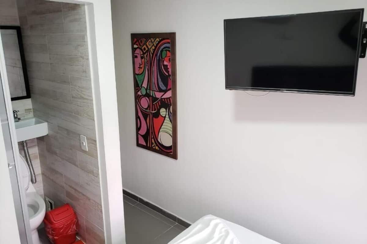 Ein Badezimmer mit Toilette, einer roten Mülltonne, einem weißen Waschbecken und einem an der Wand befestigten Fernseher.