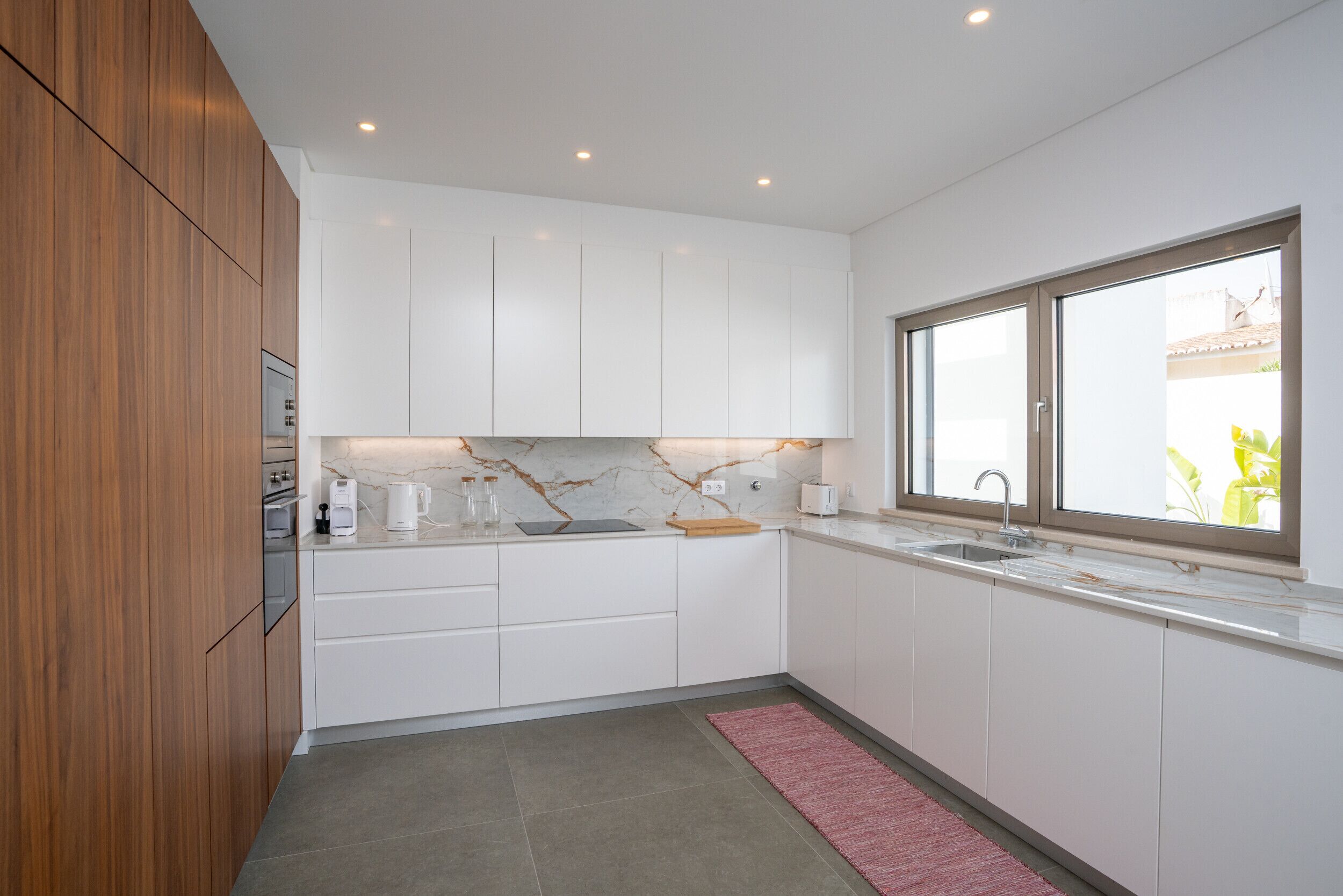Una cocina moderna con gabinetes blancos, salpicadero de mármol y una ventana que proporciona luz natural.