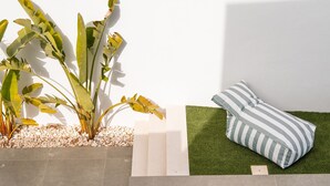A swimming pool with a tiled deck, a grassy area with a striped pillow, and a plant with broad leaves. - Bazaruto T4 swimingpool Lagos (Lagos)