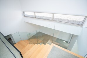 Een modern interieur met een glazen balustrade, een houten trap en uitzicht door een raam.