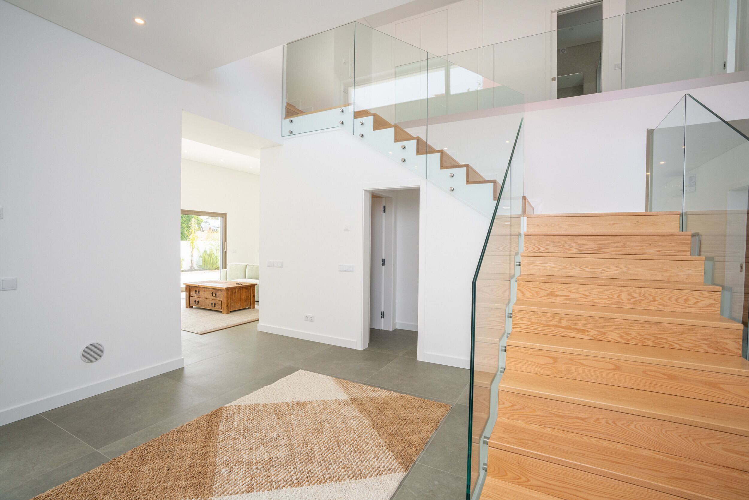Un intérieur moderne avec un escalier, des rampes en verre et une palette de couleurs neutres.