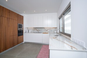 A modern kitchen with wooden cabinets, a built-in oven, white countertops, and a large window. - Bazaruto T4 swimingpool Lagos (Lagos)
